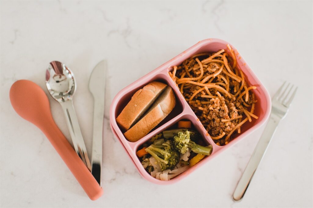 Bento Box filled with Spaghetti, broccoli, & garlic bread with utensil set on side. 