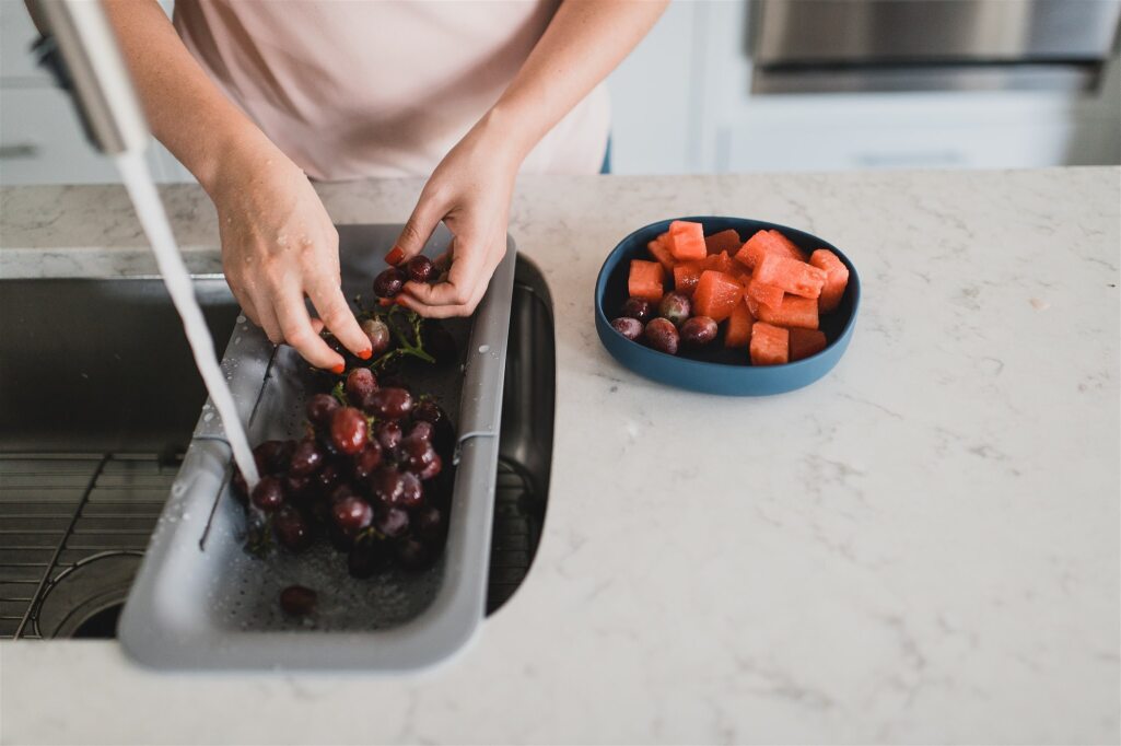 Over the sink colander with running water, rinsing grapes