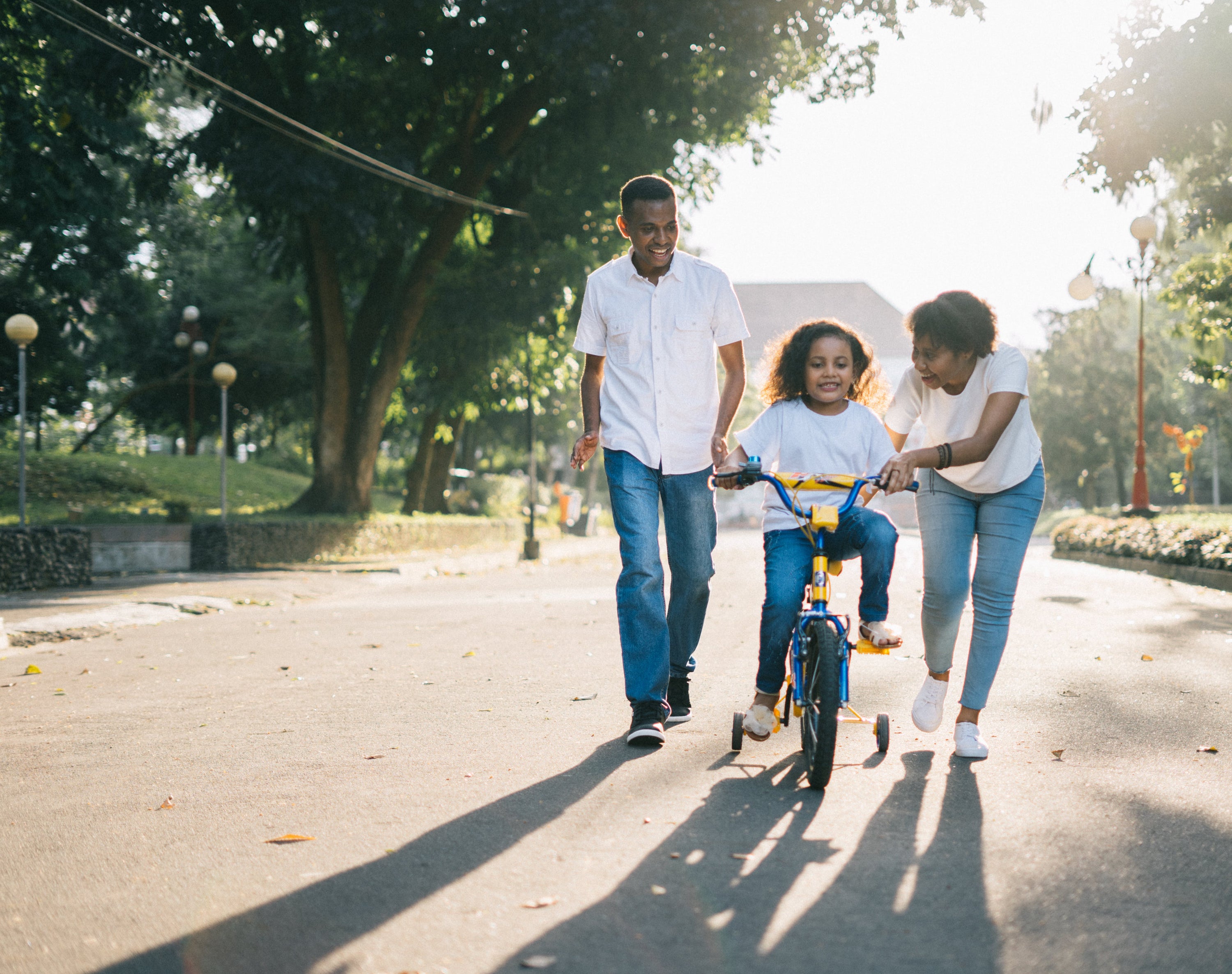 Mom & Dad teaching daughter to ride a bike with training wheels