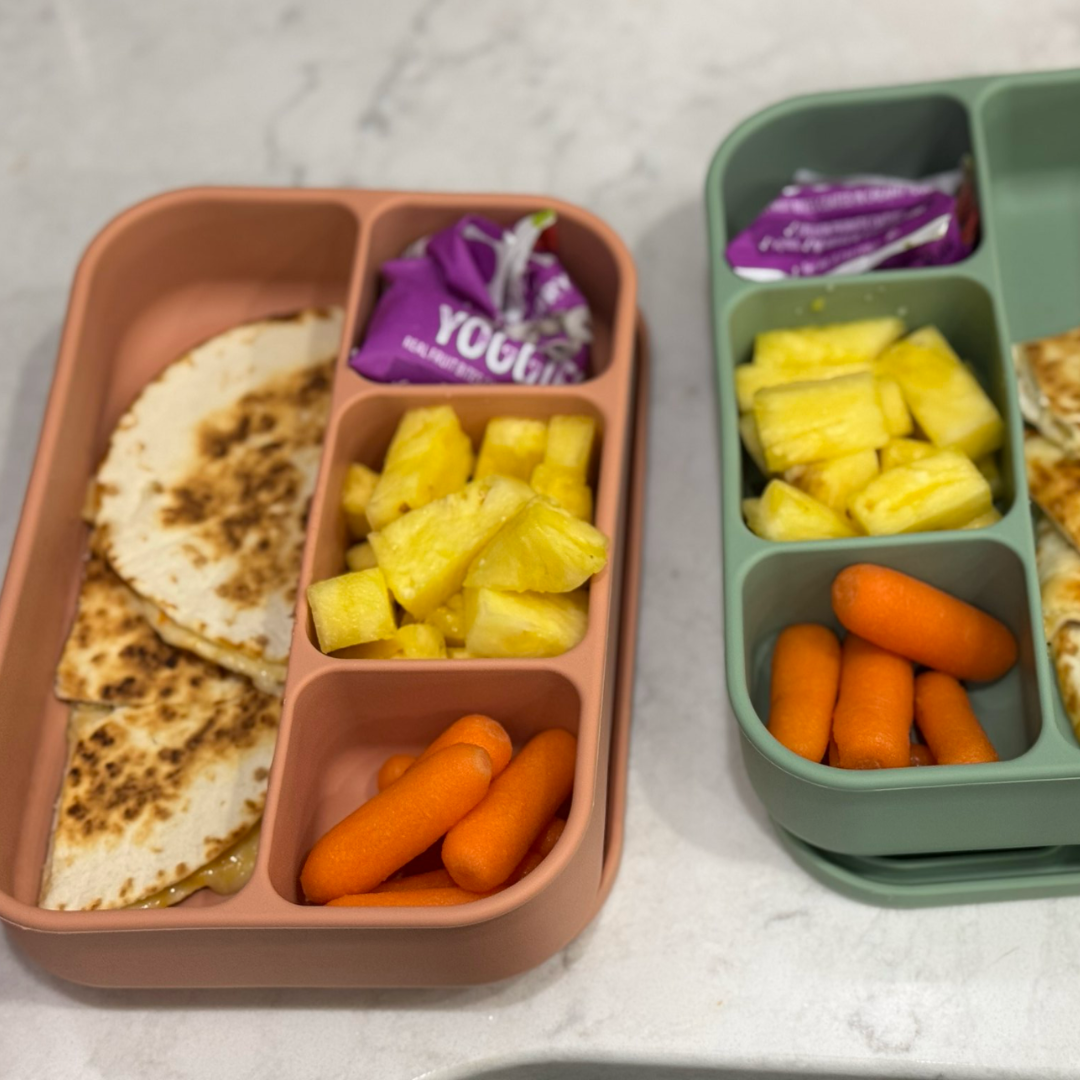 Flex Bento lunch packed with quesadilla wedges, carrot sticks, pineapple chunks, and a small sweet treat in separate compartments.